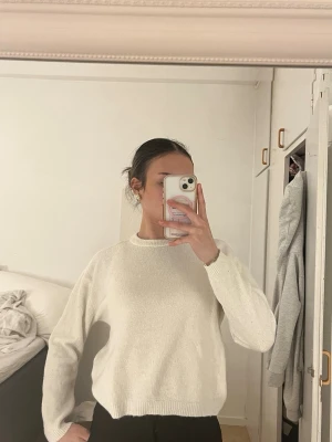 Vit stickad tröja med rund hals - En enkel och stilren vit stickad tröja med rund halsringning och långa ärmar. Tröjan har en rak passform och ribbstickade muddar vid ärmslut och nederkant. Perfekt att matcha med jeans eller kjol.