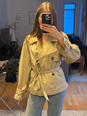 Trenchcoat  - JÄTTEfin trenchcoat/jacka/kappa i beige från Ginatricot i storlek M. Jag köpte den på Vinted men inte kommit till användning! Den har inga fläckar, är inte söndrig eller liknanande, men vet ej hur mycket tidigare ägaren har använt den! Inget som märks. Den är lite skrynklig, men fixas lätt med strykjärn. Skriv privat om du har frågor💕