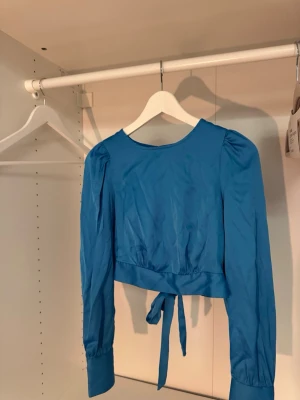 Blå långärmad topp med knyt - Snygg blå långärmad topp / blus med puffiga axlar och knyt i midjan. Toppen har en öppen detalj i ryggen och knyten, och är croppad för en trendig look. Perfekt för både fest, vardag eller finare tillställningar 💙