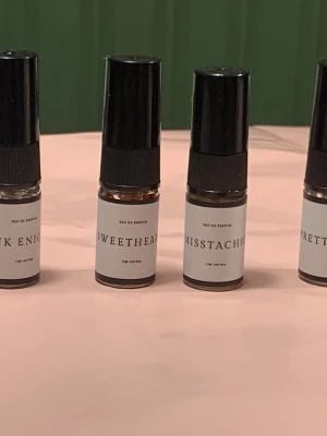 Fyra parfymprover Eau de Parfum från Curiosa - Säljer fyra små parfymprover med svarta lock och vita etiketter. Varje flaska rymmer 2 ml och har namn som Pink Enigma, Sweetheart, Misstachio och Pretty Poison.Perfekta att testa olika dofter eller ha med i väskan.