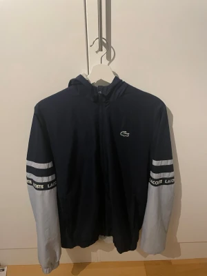 Lacoste jacka blå - Säljer då jag inte har användning för den. Jackan har en liten fläck på ena armen som ni ser på ena bilden. Där av priset på jackan. Den syns inte mycket alls när man väl bär den 