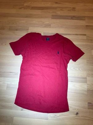 Röd t-shirt från Ralph Lauren - Röd t-shirt från Ralph Lauren med klassisk passform och korta ärmar. T-shirten har en liten blå broderad logga på bröstet och är tillverkad i mjuk bomull. Perfekt för en avslappnad och stilren look.