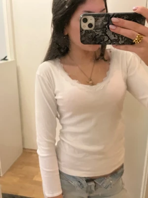 Vit långärmad topp med spets - Säljer en vit långärmad topp från Indiscreet med v-ringning och fina spetsdetaljer längs halsringningen. Säljer då den inte kommer till användning 