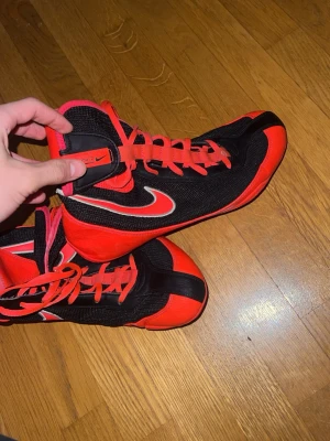 Nike machomai boxningskor röd och svart   - Säljer ett par Nike machomai boxning skor dem är i färgerna röd och svart. Skorna har snörning hela vägen upp och är tillverkade i en kombination av mesh och syntetmaterial för bra ventilation och stöd. Perfekta för träning eller match.