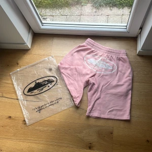 Corteiz shorts - Snygga rosa shorts med vitt tryck av en båt på ena benet. De har elastisk midja med vit snörning och är tillverkade i mjuk bomull. Perfekta för chill dagar eller när du vill ha en avslappnad look. Skick 8,5/10 🙌🏽 Mvh ItsForfits 🌟 