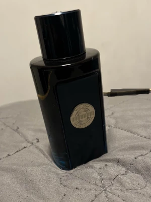 The Icon parfym från Banderas 100ml - Snygg parfymflaska i mörkblått glas med svart lock från Banderas, modellen The Icon. Flaskan har en rund silverfärgad logotyp på framsidan och rymmer 100 ml. Kommer i en stilren blå och silver kartong.