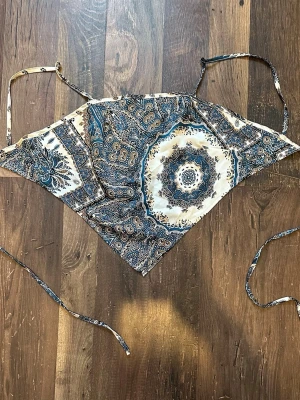 Paisleymönstrad scarf-topp i blått - Scarf-topp med paisleymönster i blått, beige och vitt. Toppen har knytband i sidorna och tunna axelband. 