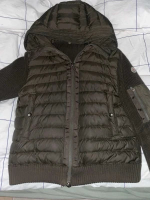 Brun pufferjacka från Moncler - Snygg grön cardigan från Moncler med stickade ärmar och huva. Jackan har dragkedja framtill, två fickor. Monclerlogga på ärmen. Perfekt för dig som gillar en jävligt fet jacka