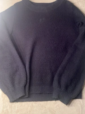 Mörkblå stickad tröja med rund hals - Mysig mörkblå stickad tröja med rund halsringning. Tröjan har ribbstickade muddar vid ärmslut och nederkant, perfekt för lager-på-lager-stil under kyliga dagar.