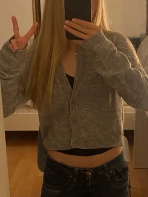 stickad kofta - Grå, mjuk och cropped kofta från H&M Divided. Koftan har v-ringning, knäppning framtill med tre knappar och ribbade muddar. Perfekt att slänga över ett linne eller t-shirt för en chill look.