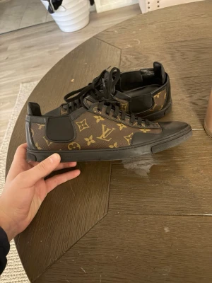 Louis Vuitton monogram sneakers (äkta) - Snygga Louis Vuitton sneakers med klassiskt brunt och svart monogrammönster. Skorna har svarta detaljer, snörning och platt sula. Tillverkade i skinn och syntetmaterial med rund tå och lågt skaft. Perfekta för dig som vill ha en lyxig touch på din outfit.