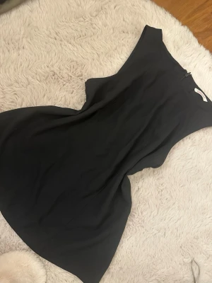 Svart ärmlös topp - Minimalistisk svart top med ärmlös design och rund hals. Toppen har en rak och loose passform som ger en clean och modern look. Perfekt för dig som gillar stilrena plagg med enkel siluett.