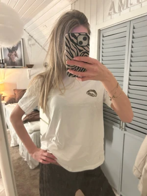 Vit t-shirt med leopardläppar från VILA - Snygg vit t-shirt från VILA med ett coolt leopardmönstrat läpptryck på bröstet. Klassisk passform med rund hals och korta ärmar. Perfekt att styla med jeans eller kjol för en trendig look.