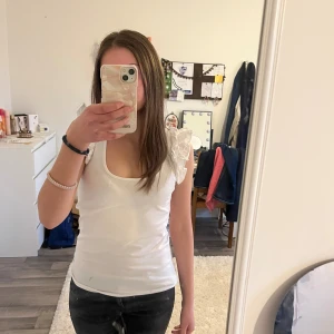 Vit linnetopp med volangärmar - Söt vit linnetopp med volangdetaljer på axlarna och djup rundringning. Perfekt för varma dagar och enkel att styla till olika looks. Tillverkad i mjukt bomullsmaterial för en bekväm känsla.