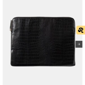 Svart datorväska i skinnimitation - 15 TUM. Stilren svart datorväska från Åhlens i skinnimitation med croco-mönstrad framsida och slät baksida. Väskan har guldfärgad dragkedja och ett innerfack för småsaker. Säljer pga att jag köpt fel storlek 