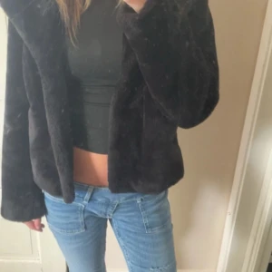 Svart pälsjacka med croppad passform - Säljer en svart pälsjacka med croppad passform och långärmade ärmar. Jackan är mjuk och fluffig. Enkel design utan synliga detaljer som knappar eller dragkedja.