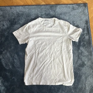 Vit t-shirt från Bläck, storlek M - En klassisk vit t-shirt från Bläck i storlek M. T-shirten har rund hals och korta ärmar, tillverkad i mjuk bomull som känns skön mot huden. Perfekt enkel stil och passar till allt. Snygg att matcha med jeans eller shorts.