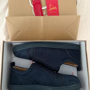 Mörkblå sneakers från Christian Louboutin - Säljer ett par mörkblå sneakers från Christian Louboutin med klassisk röd sula. Skorna har rund tå, snörning och är tillverkade i mocka med detaljer i skinn. Snygg och stilren design som sticker ut med den ikoniska röda undersidan.