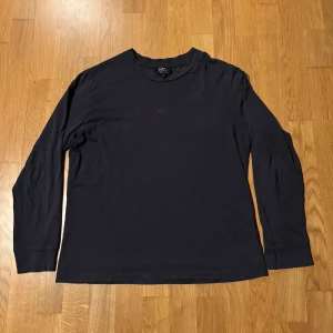 Mörkblå långärmad tröja från A.P.C. - Säljer en stilren mörkblå långärmad tröja från A.P.C. i mjuk bomull. Tröjan har rund halsringning och diskret A.P.C.-logga framtill. Perfekt för dig som gillar minimalistisk och clean stil.