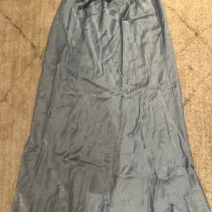 Ljusblå långkjol från NOWOMENSLABEL - Säljer en stilren ljusblå långkjol från NOWOMENSLABEL. Kjolen har en mjuk satinliknande yta och faller snyggt längs kroppen. Perfekt för dig som gillar minimalistisk och elegant stil.