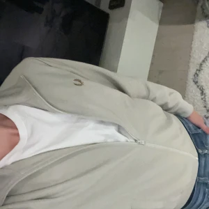 Beige Fred Perry fullzip  - Säljer en beige fullzip från Fred Perry med  klassisk logga broderad på bröstet. Modellen har hög krage, ribbade muddar och två fickor framtill. Inköpt för 1599 och skicket är desamma som då!!!