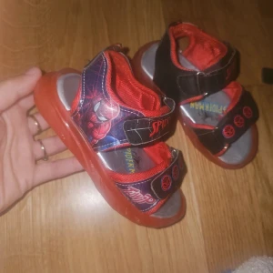 Spiderman sandaler med röd sula - Coola sandaler med belysning och Spiderman-tryck. .Skorna har justerbara kardborreband med svarta och röda spindelmotiv, samt en röd sula och röd mesh på insidan. Perfekta för alla små Spiderman-fans som vill sticka ut i sommar.