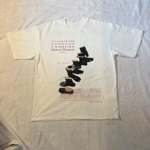 Vit Maison margiela T shirt - Maison Margiela t-shirt i vit bomull med ikoniskt tryck framtill, tabis och en halvsynlig text. Klassisk rund hals och korta ärmar. Såklart märkets signaturstygn i nacken. Storleken är 44/s men skulle säga att den sitter närmre en M. Den är från aw 02/03. Perfekt för dig som gillar statement-plagg och designer vibes. Kan mötas i Stockholm men skickar också snabbt, skriv vid minsta fråga! Modellen är 179 65kg och brukar bära S