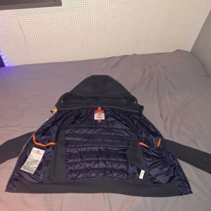 Parajumpers puffer hoodie navy S - Mörkblå pufferjacka från Parajumpers med huva och dragkedja. Jackan har quiltad framsida i glansigt material, ärmar och huva i mjukare tyg samt orange detaljer på insidan. Perfekt för kyliga dagar och snygg streetstil. Priset går att diskutera.