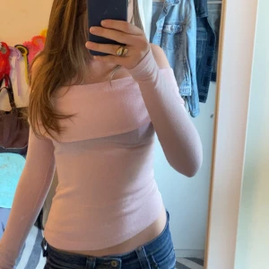 Stickad Ljusrosa offshoulder tröja - Säljer en ljusrosa offshoulder topp med långa ärmar. Toppen är tight och har en vikt kant över axlarna .