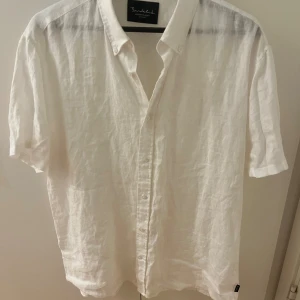 Vit linneskjorta från Bondelid L - Säljer en stilren vit skjorta från Bondelid i storlek L. Skjortan är tillverkad i svalt linne, har korta ärmar, klassisk krage och knäppning framtill. Perfekt för varma dagar när du vill ha en clean och fräsch look.