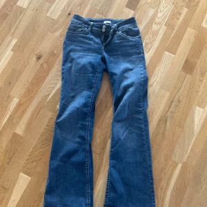 Blå bootcut jeans från Nelly - Snygga blå bootcut jeans från Nelly med klassisk femficksdesign och dubbla silverknappar i midjan. Jeansen har broderade detaljer på bakfickorna och är tillverkade i mjukt denimtyg med lätt stretch för skön passform.