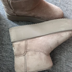 Beige platåboots från Bershka - Snygga beige boots från Bershka med platåsula och mjukt fuskpälsfoder. Skorna är i mockaimitation och har rund tå samt platt sula. Perfekta för kalla dagar när du vill vara både varm och trendig.