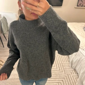 Grå stickad polotröja - Mysig grå stickad polotröja med hög krage och långa ärmar. Tröjan har en loose fit och ribbade muddar vid ärmslut och nederkant. Perfekt för kyliga dagar och enkel att matcha med jeans eller kjol.