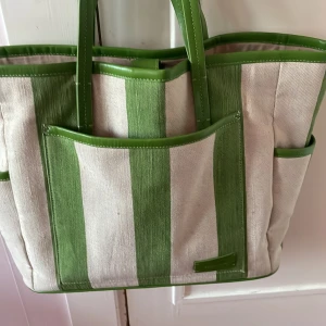 & Other Stories väska i beige och grönt.  - snygg väska från & Other Stories i grön- och beigerandig bomull med gröna detaljer i skinn. Väskan har flera ytterfack, långa och korta handtag och magnetknäppning upptill. Perfekt för att bära med sig allt man behöver under dagen. priset kan diskuteras. 