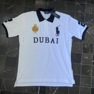 Vit Polo Ralph Lauren Piké - Jag säljer en vit pikétröja från Polo Ralph Lauren med svart krage och detaljer. Storlek M. Tröjan är fräsch och helt ny, med prislappen kvar! Hör gärna av dig om du har frågor eller vill se fler bilder på tröjan!