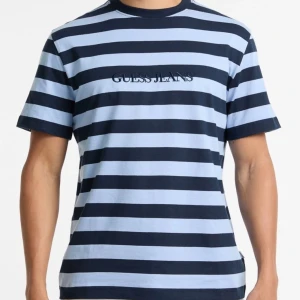 Randig t-shirt från Guess Jeans - Snygg t-shirt från Guess Jeans med breda marinblå och ljusblå ränder. Klassisk passform med korta ärmar och rund halsringning. Broderad logga på bröstet. Perfekt för en chill och stilren look.