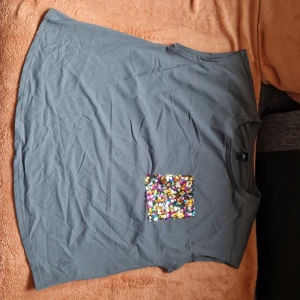 Grå ärmlös topp med paljettficka - Snygg grå ärmlös topp med en ficka av färgglada paljetter framtill. Toppen har rund halsringning och en loose passform, perfekt för dig som gillar att sticka ut med lite extra bling.