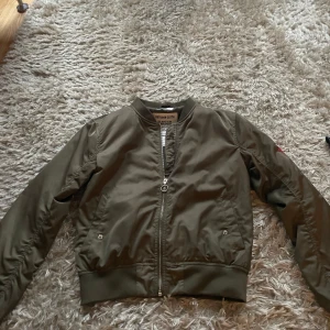 Olivgrön bomberjacka från H&M - Snygg olivgrön bomberjacka från H&M med broderad text och rosor på ryggen samt broderade läppar och texten 'Bisou' på ärmen. Jackan har dragkedja framtill, ribbade muddar och coola detaljer som ger en unik vibe. Säljer pågrund av för liten TYVÄR! Love her 😍pris går att diskutera 