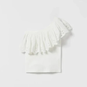Vit offshoulder topp med volang - Superfin vit offshoulder topp med bred volang och broderade detaljer. Toppen är croppad och har en axel bar, vilket ger en snygg och trendig look. Perfekt till jeans eller kjol för en fräsch sommarstil. Storken är 164 13-14 år men skulle nog passa s-xs 