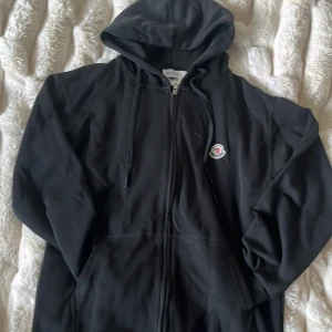 Svart hoodie från Moncler med dragkedja -  Priset är inte fast kan alltid ändra.  Den är M men passar som S.Svart hoodie från Moncler med klassisk huva, dragsko och hel dragkedja framtill. Tröjan har Moncler-logga på bröstet och är tillverkad i mjuk bomull. Perfekt för en chill och stilren look.