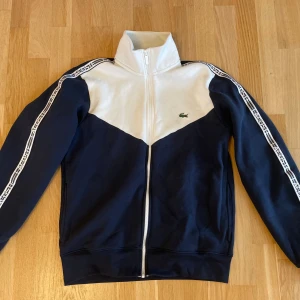 Lacoste ziptröja i blått och vitt - Snygg ziptröja från Lacoste i marinblått och vitt med dragkedja. 