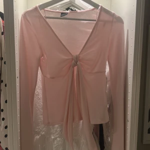 Ljusrosa långärmad topp Gina Tricot - Supersöt ljusrosa långärmad topp från Gina Tricot med v-ringning och knyt framtill. Tunn och mjuk i materialet, perfekt för lager-på-lager eller som den är. Snygg och feminin passform med långa ärmar och knyt som ger en extra detalj.