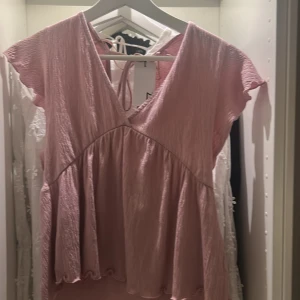 Rosa omlottklänning från 157 - PASSAR MIG SOM HAR XS. Supersöt rosa kortklänning från 157 med omlott-skärning och volangdetaljer. Klänningen har korta ärmar och knyt i ryggen. Perfekt för dig som gillar en luftig och feminin stil. Materialet är lätt och har en skrynklig struktur.