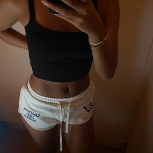 Vita shorts med tryck och snörning - Säljer ett par vita shorts med blått tryck 'California 1982 Los Angeles' på ena sidan och ’LA’ på andra. De har låg till medelhög midja och elastisk midja med snörning. Storlek S, passar även som XS 🤍