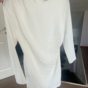 Vit långärmad kortklänning - Snygg vit klänning från NA-KD med lång ärm och enkel, stilren design. Klänningen har en lätt strukturerad yta och är kort i modellen, perfekt för dig som gillar minimalistisk stil.