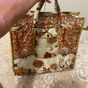 Stor blommig shoppingväska med dragkedja - En vintage rymlig shoppingväska med blommigt mönster i brunt, beige och grönt. Väskan har handtag, dragkedja för att stänga väska .ytterficka på framsidan . . Tillverkad i syntetmaterial och perfekt för att bära mycket. Mått ca 50 cm hög. Snygg vintagekänsla! . Storlek - bred :52cm - höjd :48cm .