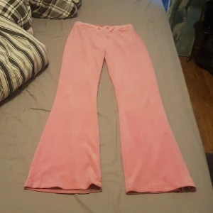 Rosa bootcut byxor från Gina Tricot XS - Säljer ett par mjuka rosa bootcutbyxor från Gina Tricot i storlek XS. Byxorna har utsvängda ben, två bakfickor med lock och är gjorda i ett skönt material som känns som velour eller polyester. Perfekta för dig som gillar färg och retrostil!