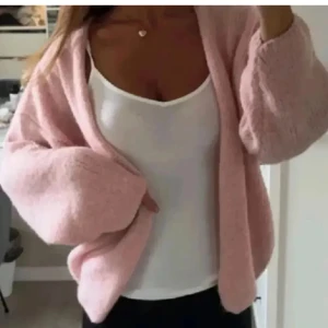 Ljusrosa stickad kofta från Lindex - Supermysig ljusrosa stickad kofta från Linsery med oversized passform och långärmade, puffiga ärmar. Koftan har öppen front utan knappar och är tillverkad i ett mjukt, fluffigt material som känns skönt mot huden. Perfekt att slänga över en topp för en chill look. LÅNAD BILD🩷 den är lite nopprig