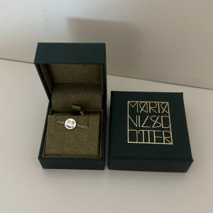 Silverarmband Maria Nilsdotter - Unikt silverarmband från Maria Nilsdotter med en rund berlock som har ett handgraverat ansikte. Kedjan är tunn och smidig, perfekt för att ge en cool och personlig touch till din stil. Frakt betalt köparen!!! Kedjan är ca 17cm 