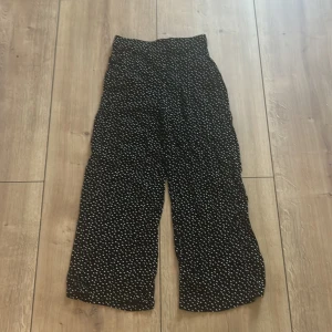 Svarta prickiga vida byxor - Svarta byxor med vita prickar och breda ben. Hög midja och loose fit för en chill och trendig look. Tunt, flowigt tyg som känns skönt mot huden. Perfekta för dig som gillar mönster och vill sticka ut lite extra.